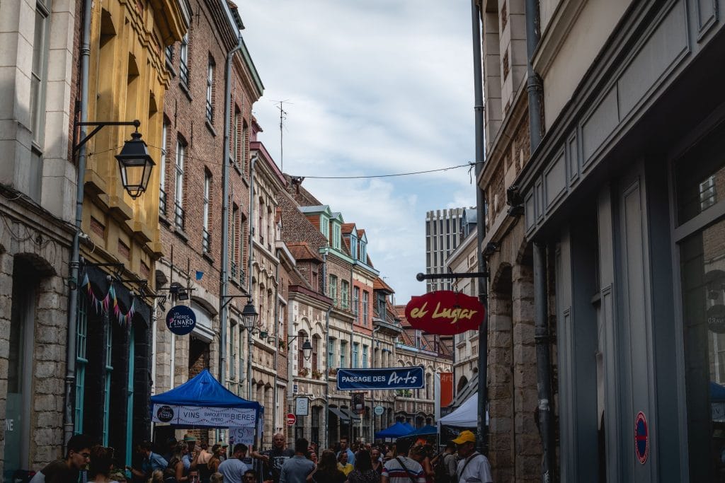 Rue commerçante du Vieux-Lille bondée, avec des stands de vente installés le long des façades de brique