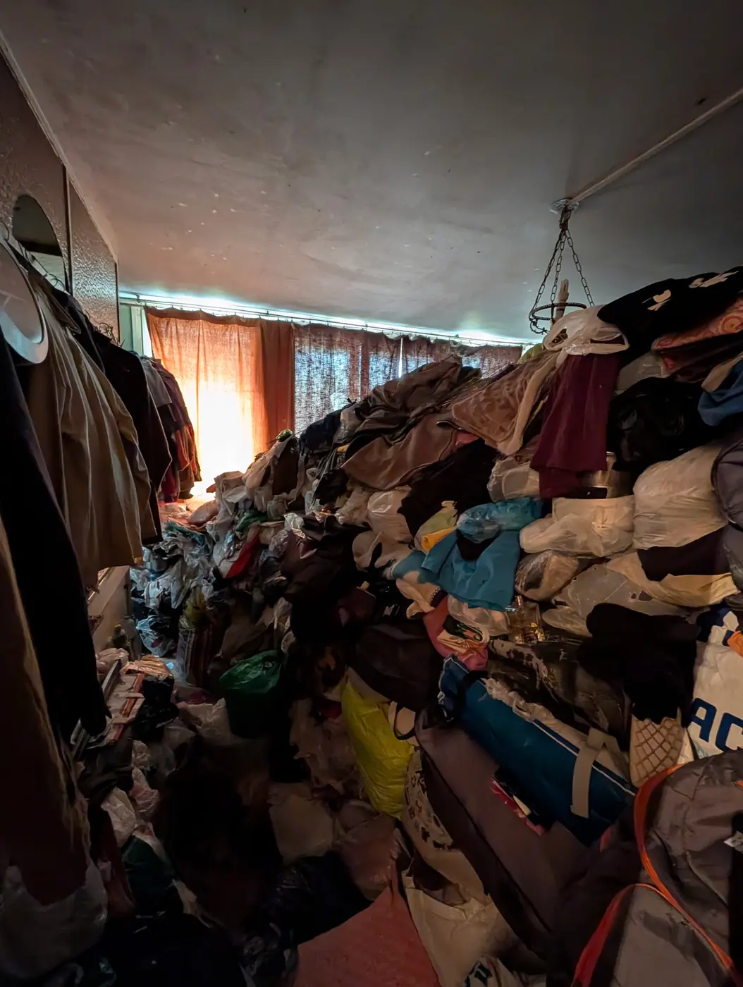 Chambre dont les vêtements et les sacs sont empilés jusqu'au plafond, ne laissant qu'un passage étroit