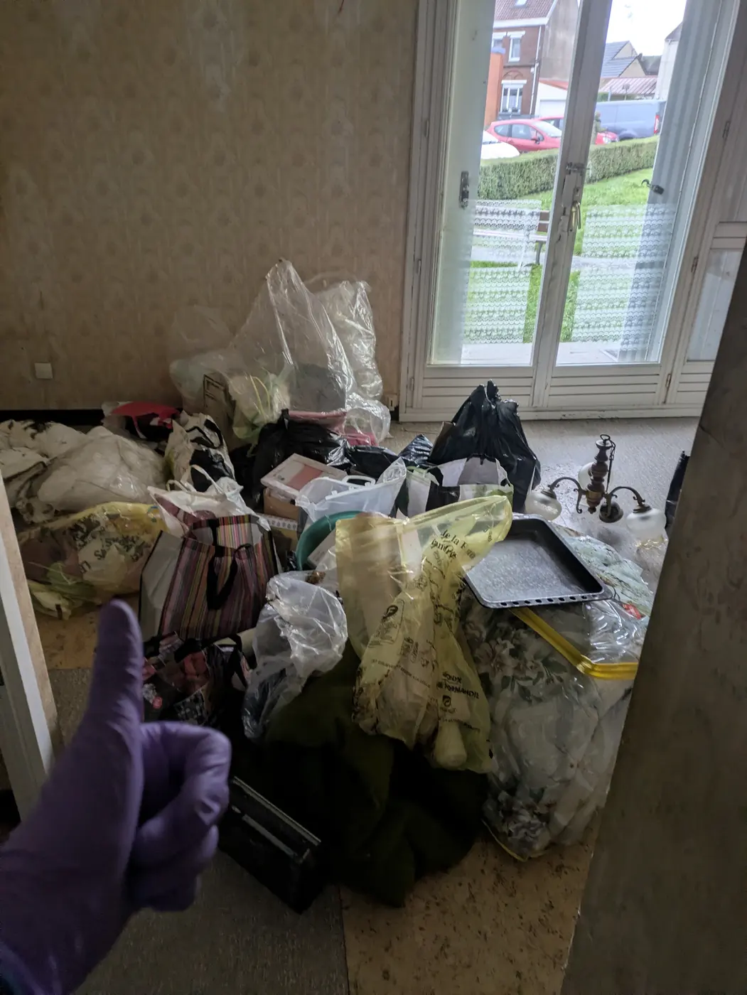 Chambre encombrée de sacs et de linge devant une fenêtre, avant l'intervention de Soli'Débarras
