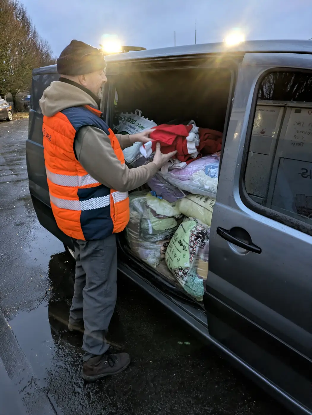 Chargement de sacs de vêtements et de linge triés dans un utilitaire, destinés au don