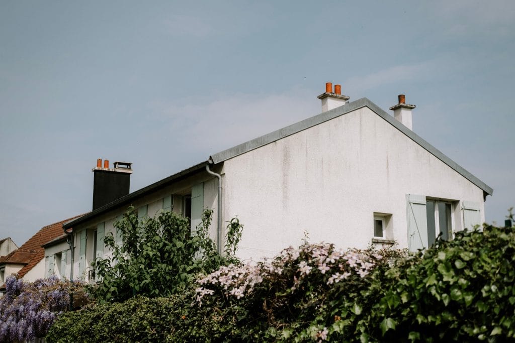 Maison de famille aux volets gris-vert, vue depuis une haie de glycine et de clématites en fleurs