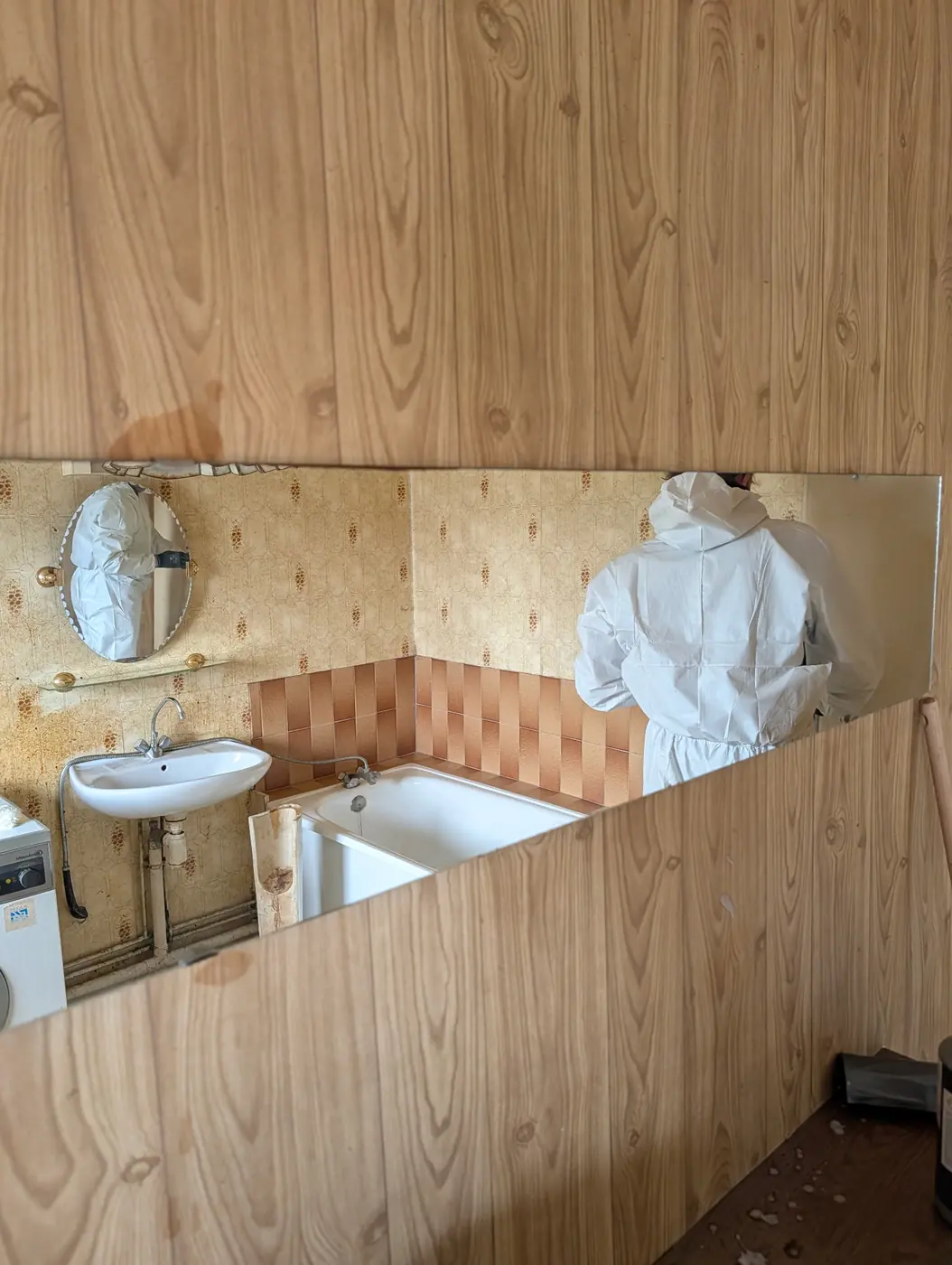 Salle de bain vétuste en cours de remise en état, avec un intervenant en combinaison de protection