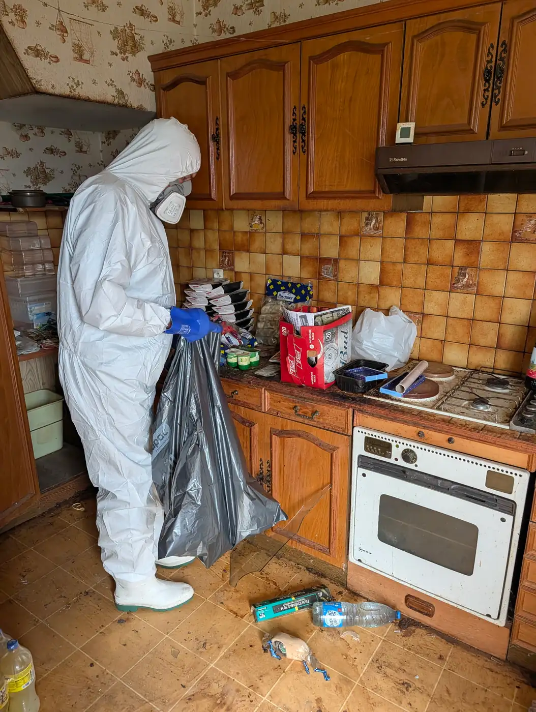 Intervenant de Soli'Débarras en combinaison intégrale et masque à cartouches, évacuant les déchets d'une cuisine insalubre