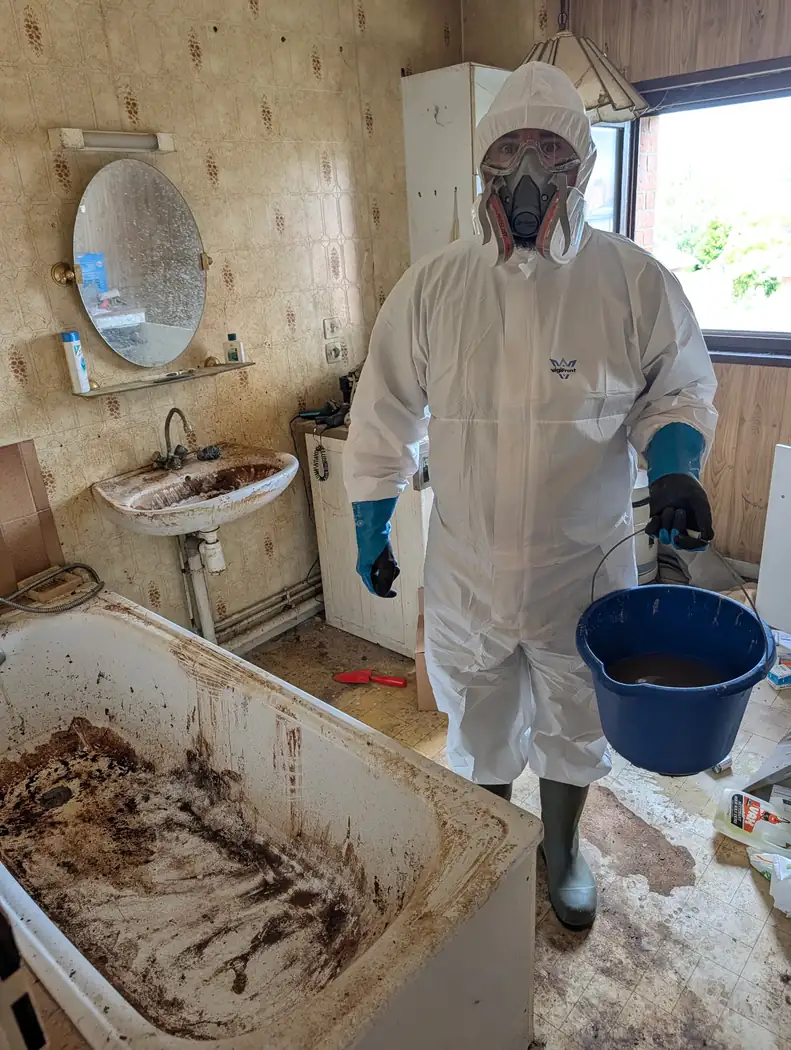 Intervenant de Soli'Débarras en combinaison, lunettes et masque, portant un seau, dans une salle de bain en cours de remise en état
